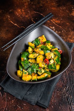 Chinese smashed cucumbers with herbs and sesame oil. Dark background. Top view.