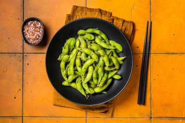 Boiled Edamame Soy Beans with sea salt and sesame seeds. Orange background. Top view.