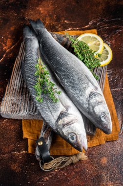 Raw Sea Bass, Branzino fish with thyme and lemon. Dark background. Top view.