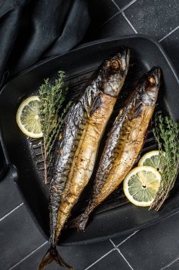 Grilled mackerel fish with lemon, herbs and spices in a skillet. Black background. Top view.