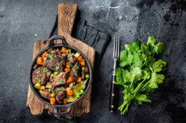 Beef stew with potato, carrot and herbs in a skillet. Black background. Top view.