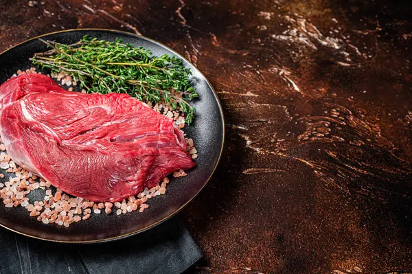 Raw beef sirloin steak with herbs and salt. Dark background. Top view. Copy space.