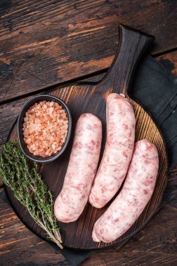 Fresh Raw Bratwurst meat sausages ready for cooking on wooden board. Wooden background. Top view.