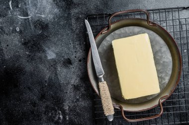 Butter block in steel kitchen tray. Black background. Top view. Copy space.