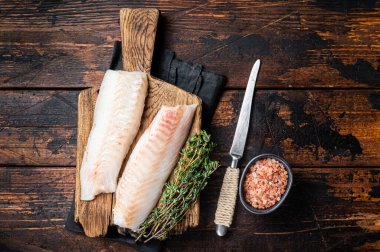 Cod fish fillets, raw codfish with thyme on wooden board. Wooden background. Top view.