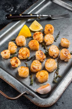 Scallops poached in a butter and garlic Sauce in a steel tray with thyme. Black background. Top view.