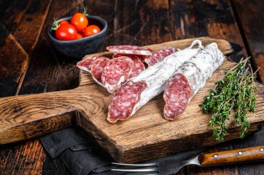 Spanish dry salami sausage Fuet on wooden cutting board. Black background. Top view.
