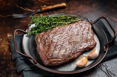 Grilled flank beef steak with herbs. Dark background. Top view.