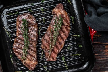 Fried denver beef meat steak with thyme in a grill skillet. Wooden background. Top view.