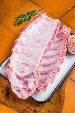 Fresh Raw pork spare loin ribs in a steel tray with herbs. Orange background. Top view.
