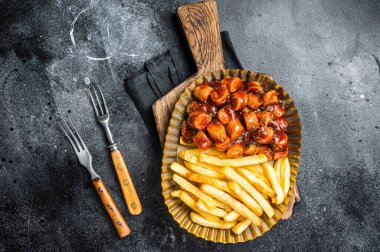 German currywurst with french fry served in a steel plate. Black background. Top view.