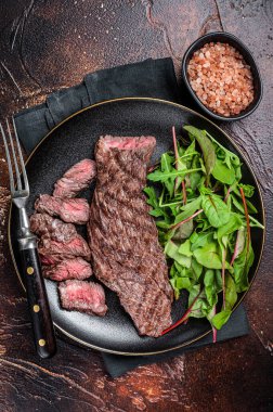 Juicy Grilled Machete skirt beef meat steak on plate with salad. Dark background. Top view.