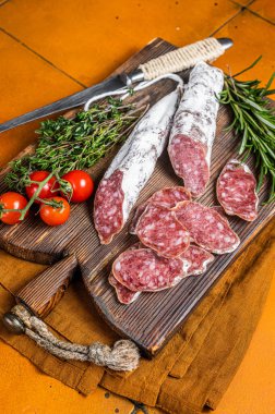 Spanish Fuet sausage slices on wooden cutting board. Orange background. Top view.