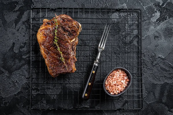 Grilled Striploin beef meat steak or new york steak on a grill rack. Black background. Top view.