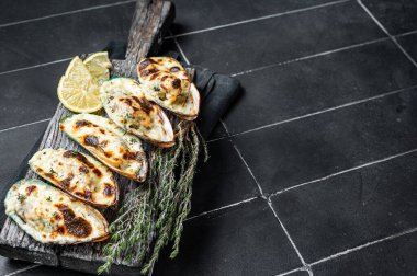 Mussels in Roquefort cheese sauce in shells on wooden board. Black background. Top view. Copy space.