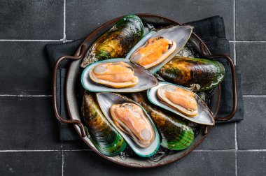 Large green mussels in shells on tray with ice. Black background. Top view.