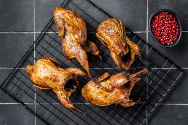 Grilled whole quails with herbs and spices. Black background. Top view.