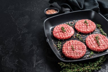Raw Ground beef meat Burger steak cutlets in grill skillet ready for cooking. Black background. Top view. Copy space.