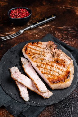 Roast BBQ pork Chop or T-bone meat steak sliced on a board. Dark background. Top view.