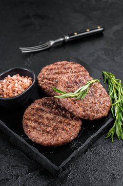 Beef burger patty cutlet for hamburger grilled on BBQ on marble board with rosemary. Black background. Top view.
