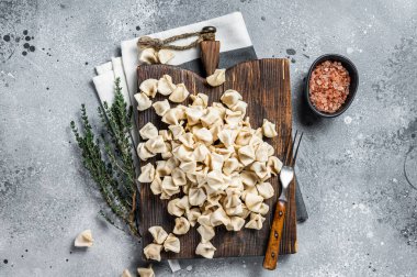 Uncooked Manti Dumpling on wooden board with herbs, raw food. Gray background. Top view.