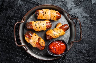 Pigs in Blanket puff pastry sausage wrap roll. Black background. Top view.