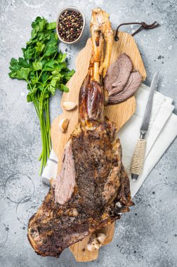 Whole roast mutton lamb leg with spices on a wooden board. Gray background. Top view.