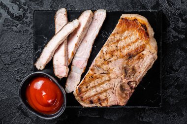 Grilled slised pork Chop or T-bone meat steak. Black background. Top view.