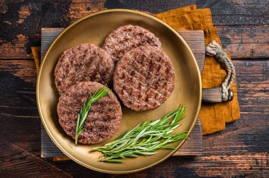 Grilled burger beef meat patty with herbs and spices on steel plate. Wooden background. Top view.