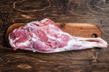 Mutton meat. Raw whole lamb leg thigh on butcher board. Wooden background. Top view.