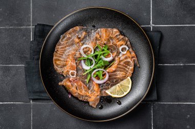 Fresh Salmon carpaccio with onion and arugula on a plate. Black background. Top view.
