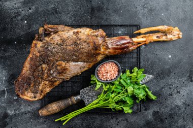 BBQ Roasted lamb mutton leg with herbs and spices on a grill. Black background. Top view.