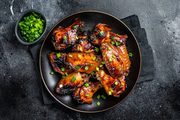 Baked chicken wings with sweet chili sauce in a plate. Black background. Top view.