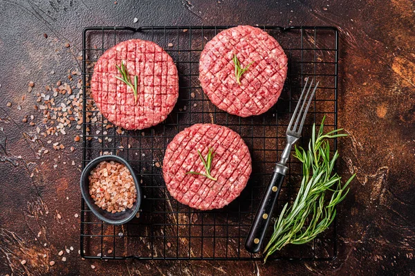 Raw burger cutlet from beef meat with spices and rosemary ready for cooking. Dark background. Top view.