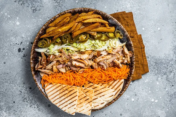 Chicken Shawarma Doner kebab on a plate with french fries, vegetables and salad. Gray background. Top view.
