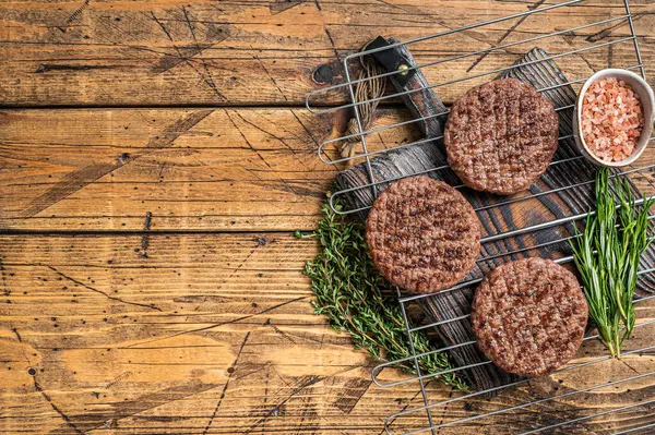 BBQ Grilled burger beef meat steak on grill with herbs. Wooden background. Top view. Copy space.
