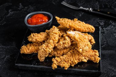 Breaded chicken strips Fingers with Ketchup. Black background. Top view.