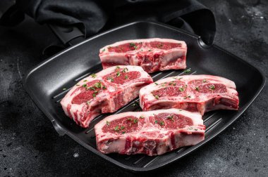 Raw lamb loin rib chops steaks in grill skillet with rosemary and thyme. Black background. Top view.