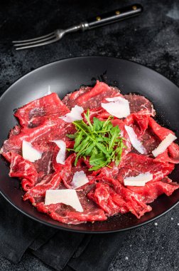 Beef Carpaccio cold appetizer with parmesan and arugula on a plate. Black background. Top view.