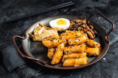 Tteokbokki, Topokki stick rice cake in Hot and spicy sauce with egg and mashrooms. Black background. Top view.