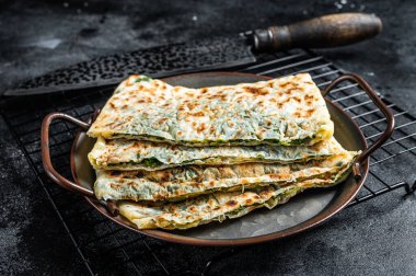 Gozleme Turkish flatbread with greens and cheese. Black background. Top view.