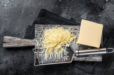 Grated cheese for cooking on a cutting board . Black background. Top view.