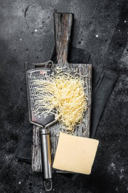 Grated cheese for cooking on a cutting board . Black background. Top view.