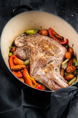Roasted lamb mutton shoulder meat in a baking dish with vegetables. Black background. Top view.