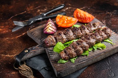 Turkish adana kebab, ground beef and lamb meat grilled on skewers served with tomato, salad and onion. Dark background. Top view.