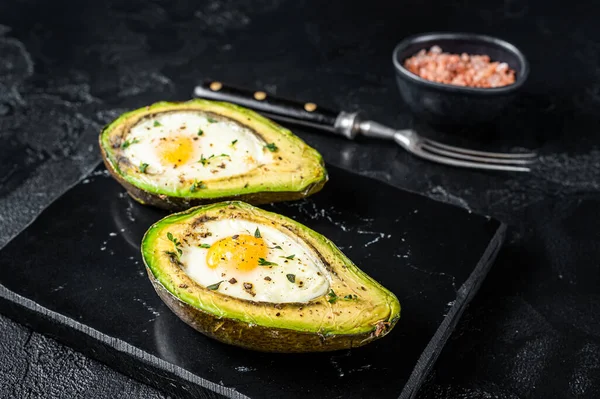 Eggs baked in avocado with herbs and spices. Black background. Top view.