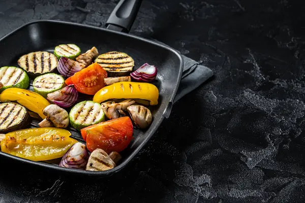 Vegetables grilled in a grill skillet, bell pepper, zucchini, eggplant, onion and tomato. Black background. Top view. Copy space.