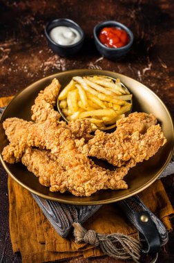 Dip fried Chicken breast strips with French Fries and sauces. Dark background. Top view.