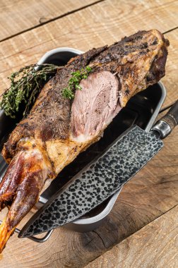 Whole oven roasted goat leg meat with thyme in a steel tray. Wooden background. Top view.