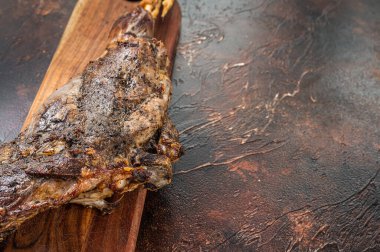 Roast lamb leg meat with herbs and spices on a cutting board. Dark background. Top view. Copy space.